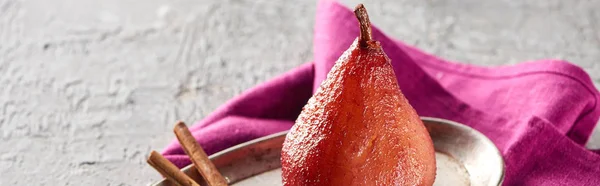 Délicieuse poire dans le vin à la cannelle sur plaque argentée sur surface en béton gris avec serviette rose, vue panoramique — Photo de stock