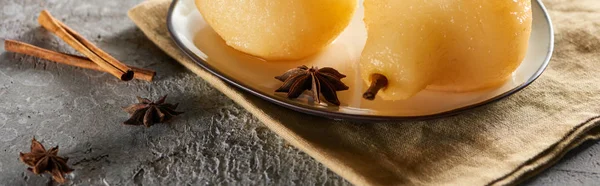 Delicious pear in wine with anise and cinnamon served on plate on napkin on grey concrete surface, panoramic shot — Stock Photo
