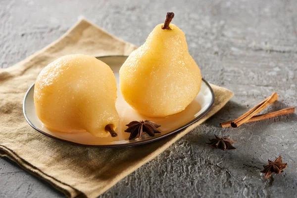 Delicious pear in wine with anise and cinnamon served on plate on napkin on grey concrete surface — Stock Photo