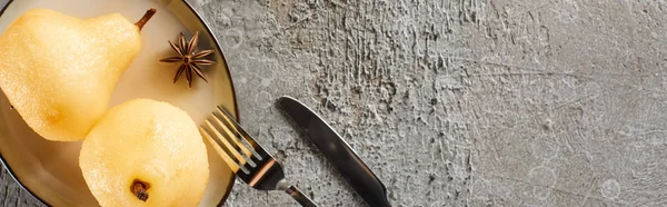 Top view of delicious pear in wine with anise served on plate with knife and fork on grey concrete surface, panoramic shot — Stock Photo