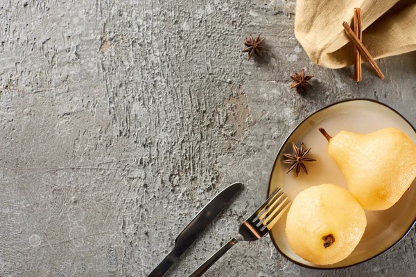 Top view of delicious pear in wine with cinnamon and anise served on plate on napkin with knife and fork on grey concrete surface — Stock Photo