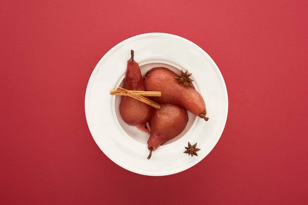 Vista superior de la deliciosa pera en vino con canela y anís en el plato sobre fondo rojo - foto de stock