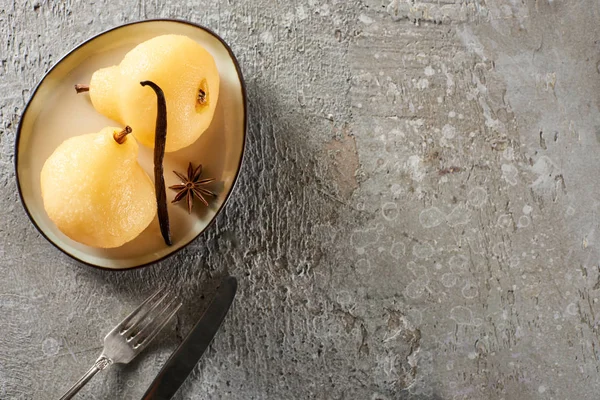 Vue de dessus de délicieuse poire dans le vin servi avec de l'anis sur l'assiette près de couverts sur la surface en béton gris — Photo de stock