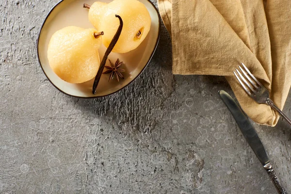 Vista superior de la deliciosa pera en vino servido con anís en el plato cerca de cubiertos y servilleta en la superficie de hormigón gris - foto de stock