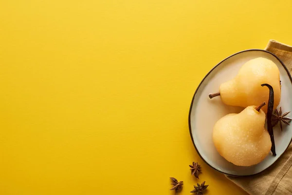 Vista superior de la deliciosa pera en vino con anís en el plato cerca y servilleta sobre fondo amarillo - foto de stock