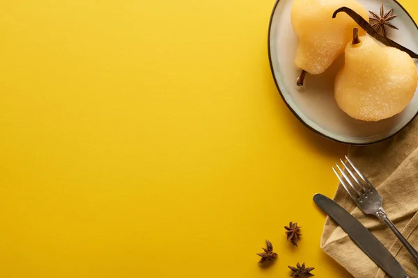 Vista superior de la deliciosa pera en vino con anís en el plato cerca de cubiertos y servilleta sobre fondo amarillo — Stock Photo