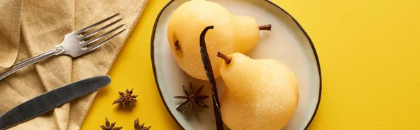Vue du dessus de délicieuse poire dans le vin avec anis sur l'assiette près de couverts et serviette sur fond jaune, vue panoramique — Photo de stock