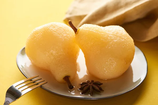 Selective focus of delicious pear in wine on plate with anise near napkin and fork on yellow background — Stock Photo