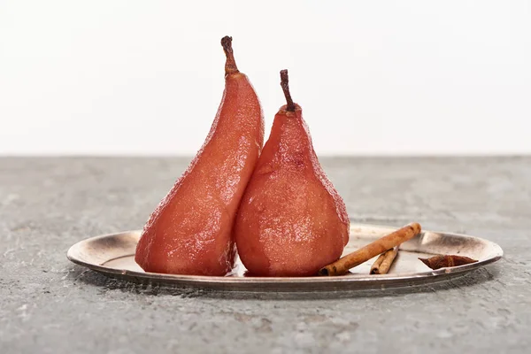 Delicious pear in wine with cinnamon and anise on silver plate on grey concrete surface isolated on white — Stock Photo