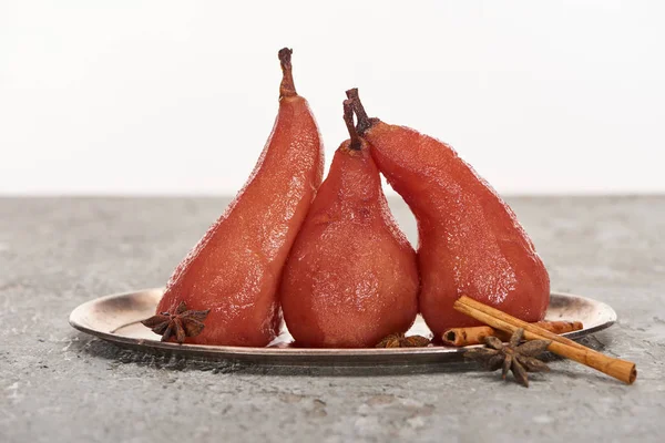 Delicious pear in wine with cinnamon and anise on silver plate on grey concrete surface isolated on white — Stock Photo