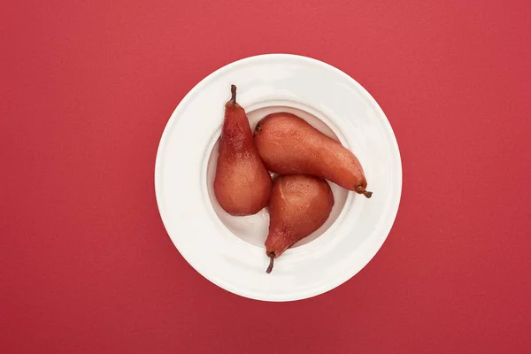 Vista superior de deliciosas peras en vino en plato sobre fondo rojo - foto de stock