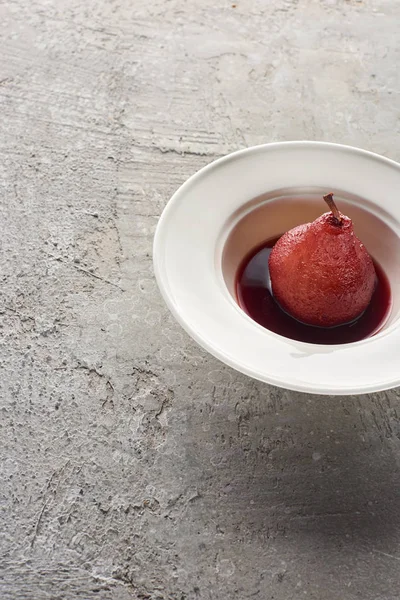 Délicieuse poire en vin rouge dans une assiette sur une surface en béton gris — Photo de stock