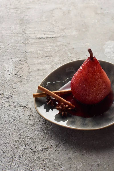 Deliziosa pera in vino rosso con cannella e anice su piatto su superficie di cemento grigio — Foto stock