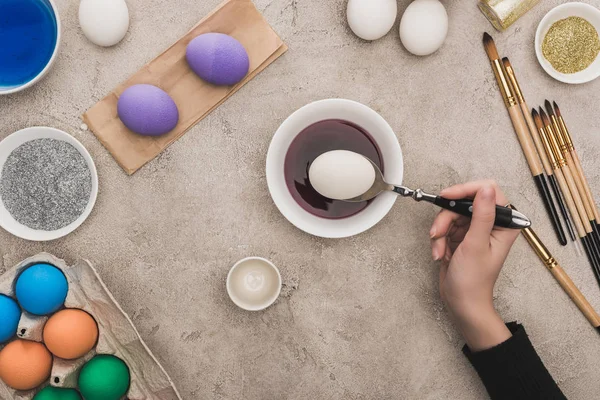 Cropped view of woman coloring chicken eggs in watercolor paints on grey concrete surface — Stock Photo