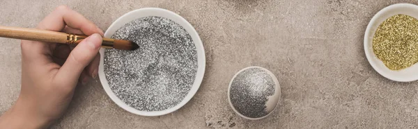 Vista recortada de la mujer decorando huevo de gallina con brillo de plata en la superficie de hormigón gris, tiro panorámico - foto de stock