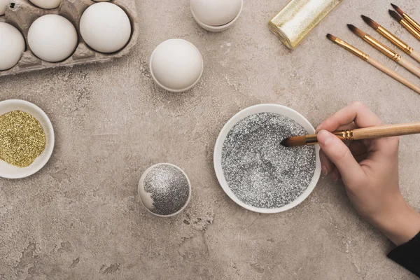 Vista cortada da mulher decorando ovo de galinha com brilho de prata na superfície de concreto cinza — Fotografia de Stock