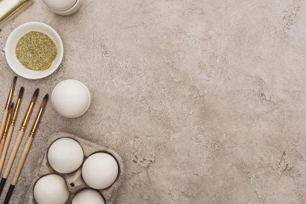 Vue de dessus des œufs de poule, paillettes dorées avec pinceaux sur la surface en béton gris — Photo de stock