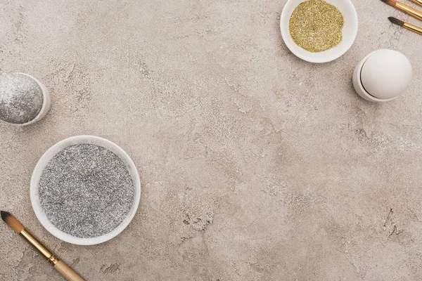 Vue de dessus des œufs de poulet, argent et paillettes dorées avec pinceaux sur la surface en béton gris — Photo de stock