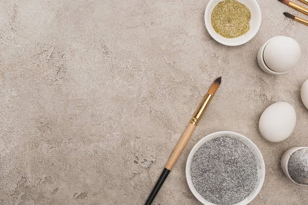 Vue de dessus des œufs de poulet, argent et paillettes dorées avec pinceaux sur la surface en béton gris — Photo de stock