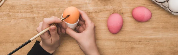 Vista ritagliata della donna che colora le uova di Pasqua con pennello al tavolo di legno, colpo panoramico — Foto stock