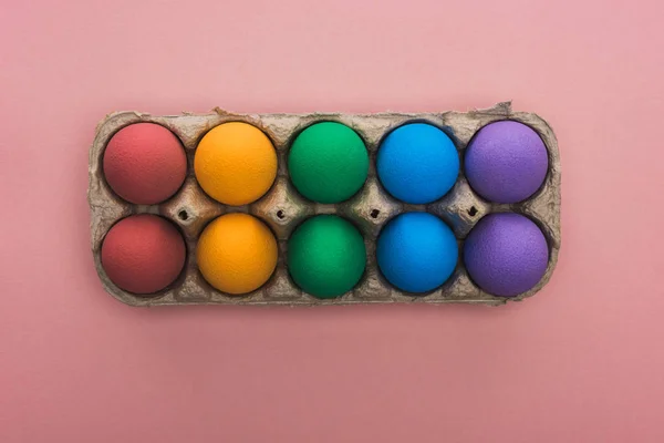 Верхний вид окрашенных пасхальных яиц в картонную коробку на розовом фоне — стоковое фото