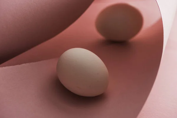 Selective focus of chicken eggs in shadow in spiral paper pink swirls — Stock Photo