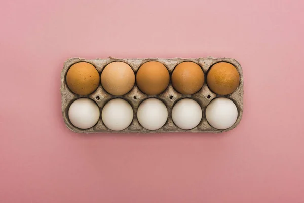 Vista superior de ovos de galinha em caixa de papelão sobre fundo rosa — Fotografia de Stock