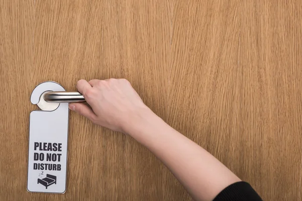 Cropped view of woman holding door handle with please do no disturb sign — Stock Photo