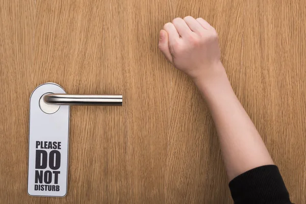 Cropped view of woman knocking at door with please do no disturb sign — Stock Photo