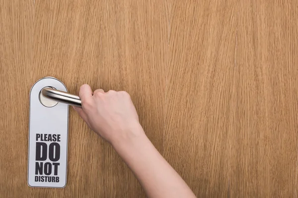 Cropped view of woman holding door handle with please do no disturb sign — Stock Photo