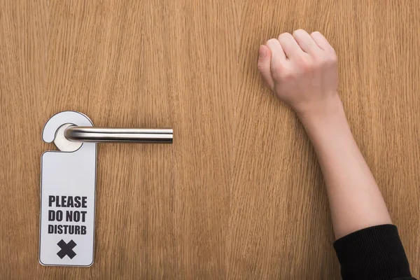 Cropped view of woman knocking at door with please do no disturb sign — Stock Photo