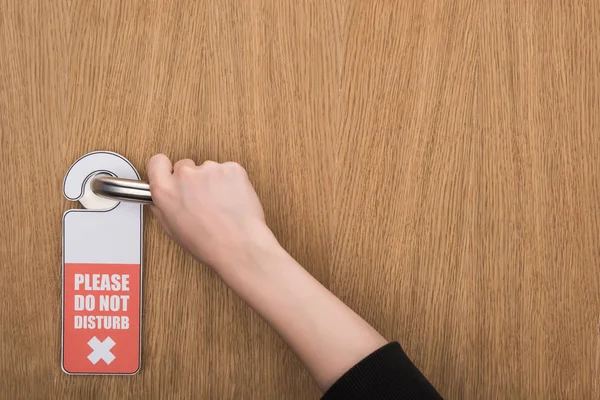 Partial view of woman holding door handle with please do no disturb sign — Stock Photo