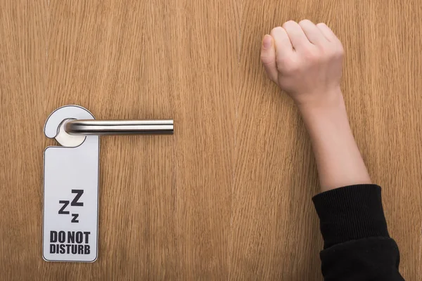 Cropped view of woman knocking at door with do no disturb sign — Stock Photo