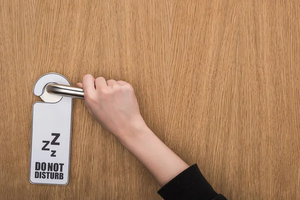 Partial view of woman holding door handle with do no disturb sign — Stock Photo