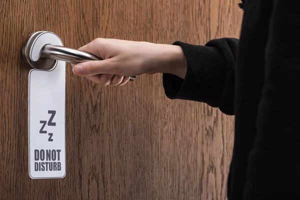 Partial view of woman holding door handle with do no disturb sign — Stock Photo