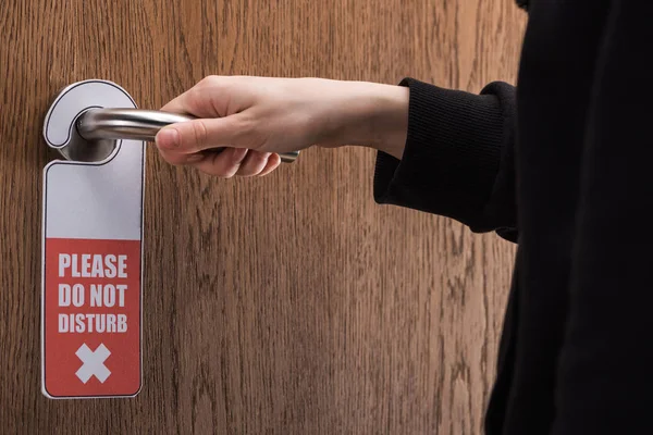 Partial view of woman holding door handle with please do no disturb sign — Stock Photo