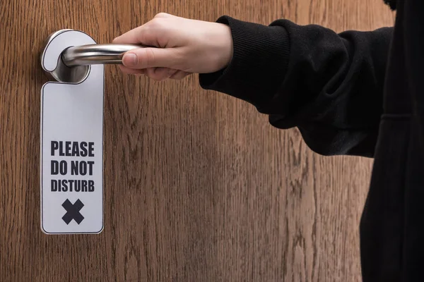 Partial view of woman holding door handle with please do no disturb sign — Stock Photo