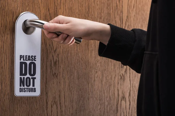 Vista recortada de la mujer sosteniendo la manija de la puerta con por favor no molestar signo - foto de stock