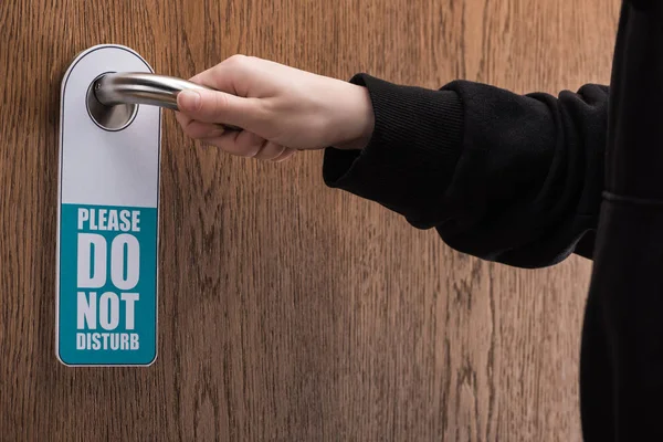 Cropped view of woman holding door handle with please do no disturb sign — Stock Photo