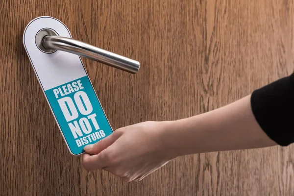 Cropped view of woman holding please do no disturb sign on hotel door — Stock Photo