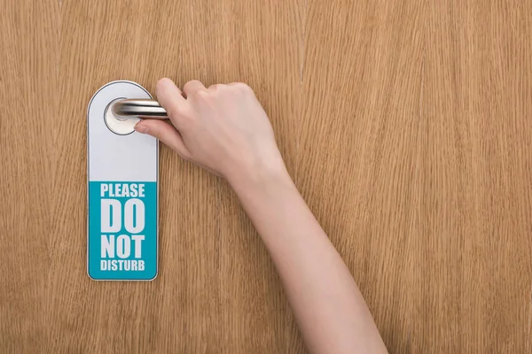 Cropped view of woman holding door handle with please do no disturb sign — Stock Photo