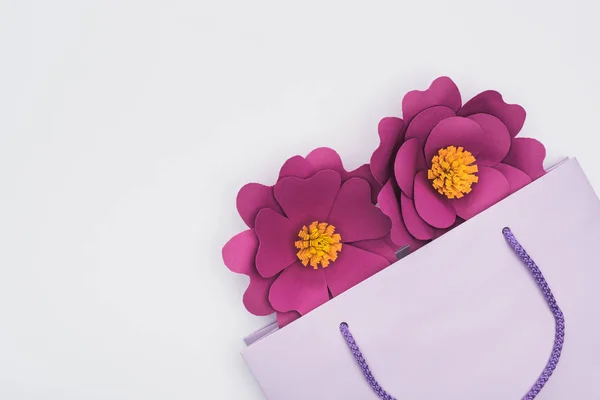 Vista superior de flores cortadas de papel en una bolsa de compras violeta aislada en blanco - foto de stock
