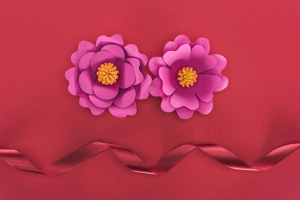 Top view of paper pink paper flowers and red silk ribbon on red — Stock Photo