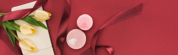 Draufsicht auf Tulpen mit Seidenband, Macarons und leerem Notizbuch isoliert auf Rot, Panoramaaufnahme — Stockfoto