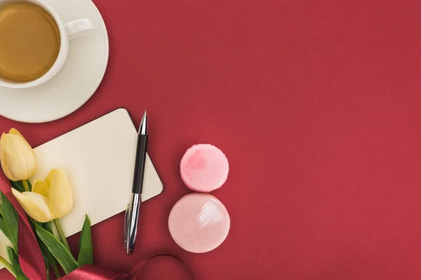 Draufsicht auf Tulpen mit Seidenband, Macarons und leerem Notizbuch in der Nähe von Kaffee isoliert auf Rot — Stockfoto