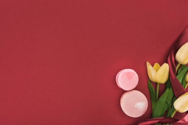 Top view of tulips with silk ribbon and pink macarons isolated on red — Stock Photo
