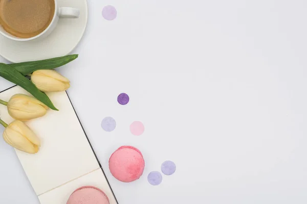 Draufsicht auf Tulpen, Macarons, leeres Notizbuch und Kaffee isoliert auf Weiß — Stockfoto