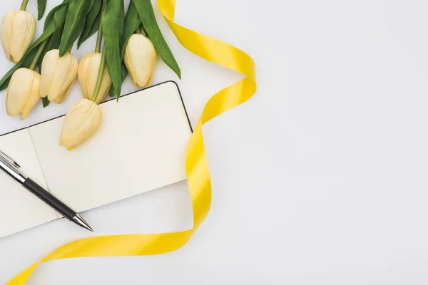 Vue du haut des tulipes, ruban jaune et bloc-notes vierge avec stylo isolé sur blanc — Photo de stock