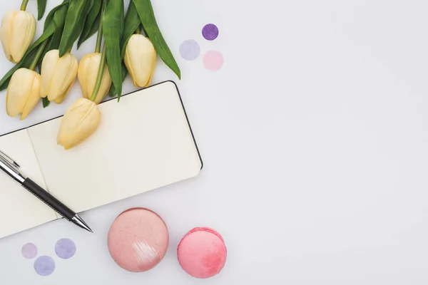 Vue de dessus des tulipes, macarons, cahier vide et stylo isolé sur blanc — Photo de stock