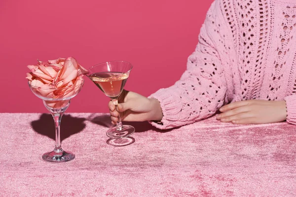 Vue recadrée d'une femme tenant un verre de vin de rose près d'un verre avec des pétales de rose sur un tissu de velours isolé sur un concept rose et féminin — Photo de stock